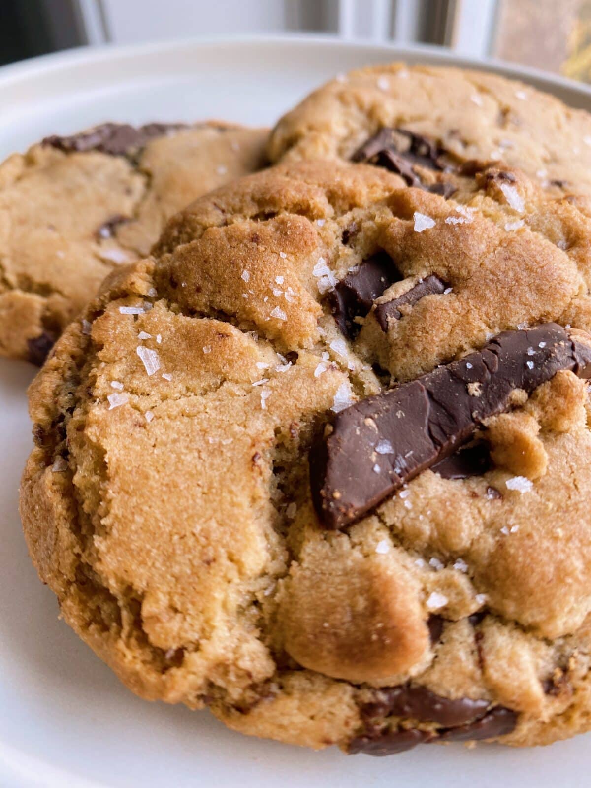 Close-up of three chocolate chip cookies topped with sea salt on a white plate.